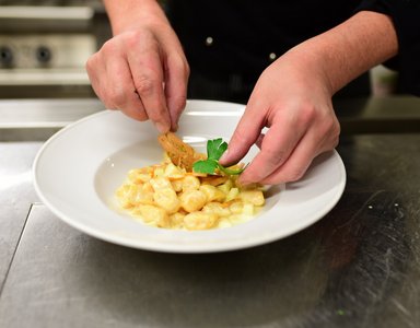 Koch richtet Nudeln mit Soße und Garnitur auf weißem Teller an