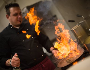 Koch entfacht Flammen beim Braten in einer Küche