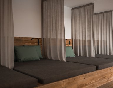 Mehrere Holzliegen mit Vorhängen und grünen Kissen in einem Raum