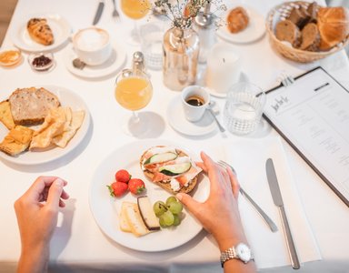 Frühstückstisch mit Brötchen, Käse, Obst und Getränken auf weißem Tuch