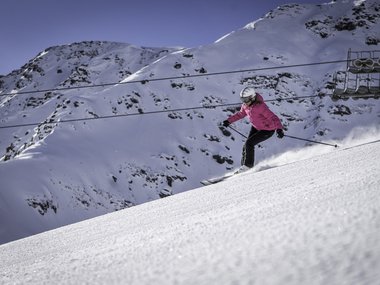 Donna con giacca rosa scia su pendio innevato sotto cielo limpido