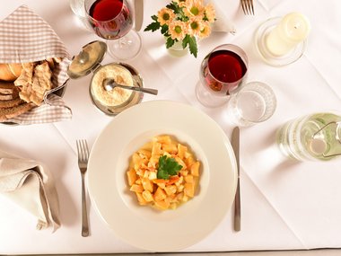 Plate of gnocchi, bread, parmesan, red wine and candle on set dining table