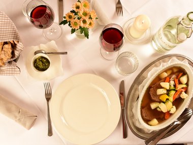 Table set with red wine, bread, vegetables, and meat dish