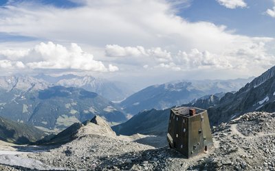 Mountain landscape with modern shelter on rocky peak under cloudy sky