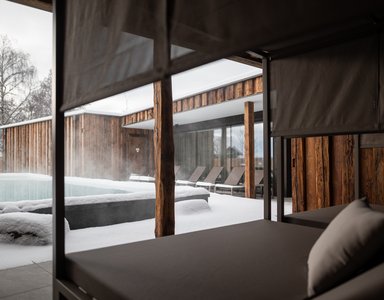 Beheizter Pool mit Schnee auf Holzterrasse und Liegestühlen im Winter