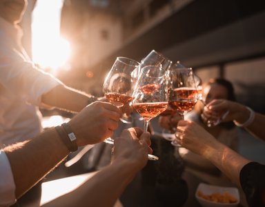 Personen stoßen mit Weingläsern voller Roséwein bei Sonnenuntergang an