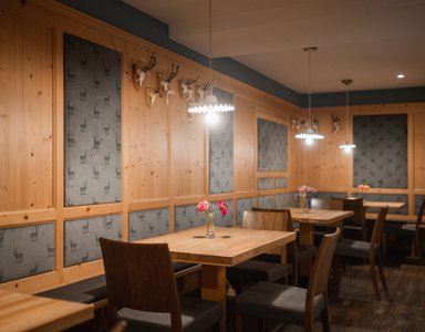 Gemütlicher Gastraum mit Holztischen, Stühlen und Hirschgeweih-Dekor an der Wand