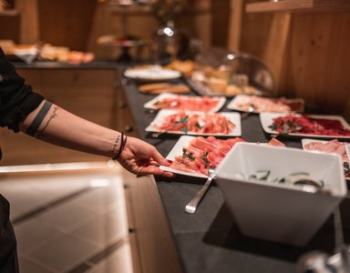 Person nimmt Teller mit Aufschnitt vom Buffet mit verschiedenen Fleischsorten
