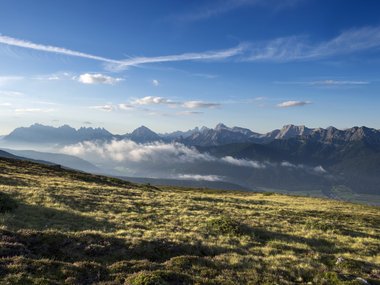 Bergwiese mit Blick auf bewölkte Berge und blauen Himmel