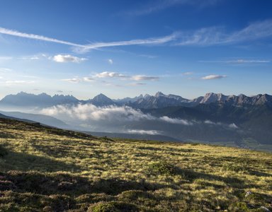 Bergwiese mit Blick auf bewölkte Berge und blauen Himmel