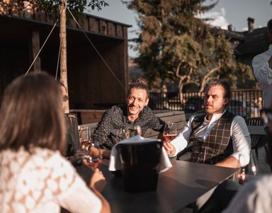 Gruppe von Freunden trinkt Wein und unterhält sich im Freien bei sonnigem Wetter