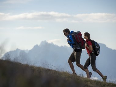 Zwei Wanderer mit Rucksäcken steigen einen Hügel bei Bergblick hinauf