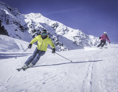 Zwei Skifahrer auf verschneiter Piste vor Bergkulisse