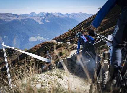 Mountainbiker fahren auf einem schmalen Bergpfad mit Alpenpanorama im Hintergrund