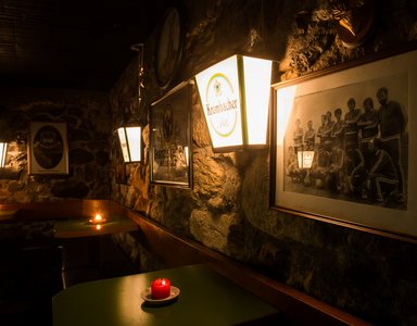 Dunkle Kneipe mit Kerzenlicht, Bierwerbung und Gruppenfoto an Steinwand
