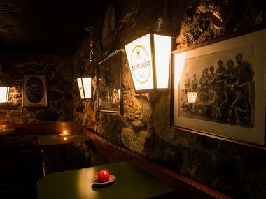 Bar buia con luci di candela, pubblicità di birra e foto di gruppo su muro di pietra