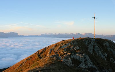 Summit cross on mountain with sea of fog and Alps at sunset