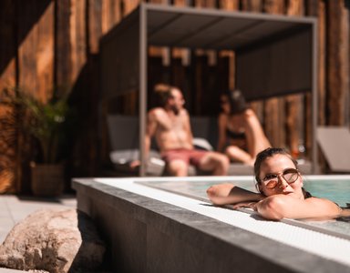 Frau entspannt im Pool, zwei Personen sitzen auf Liege im Hintergrund