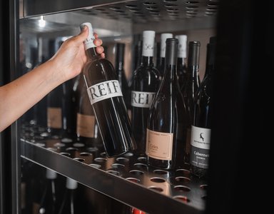 Hand nimmt eine Flasche Rotwein aus einem Weinkühlschrank