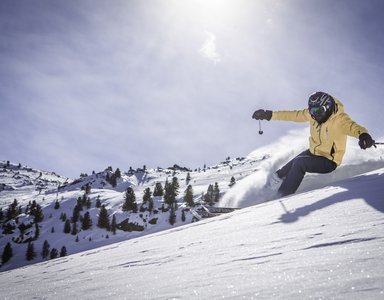 Skifahrer in gelber Jacke fährt einen schneebedeckten Hang hinunter bei Sonnenschein