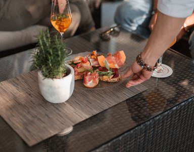 Hand greift nach Teller mit Antipasti und Weinglas auf Glas-Tisch