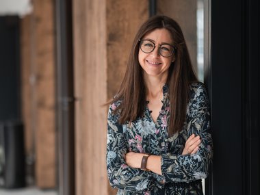 Donna con occhiali sorride e si appoggia alla parete con le braccia incrociate