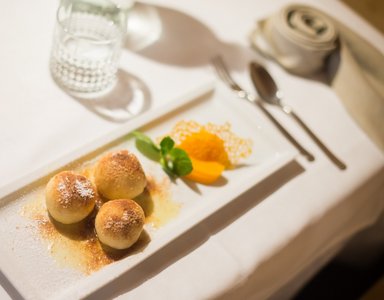 Drei Süßspeisenbällchen mit Puderzucker und Frucht auf weißer Platte