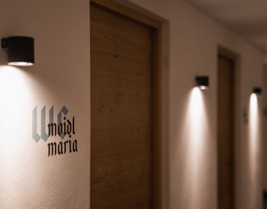 Beleuchteter Hotelflur mit Holz-Zimmertüren und Raumname an der Wand