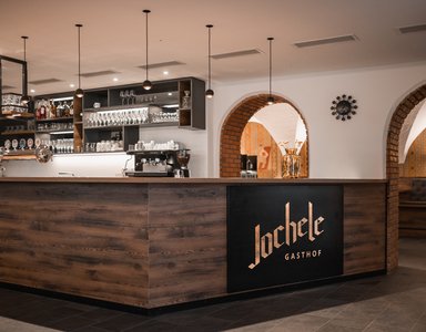 Moderne Bar mit Holztheke und beleuchtetem Logo in einem Gasthof
