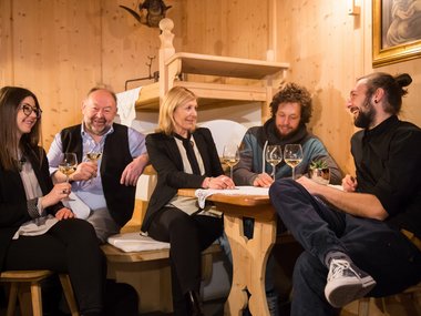 Cinque persone sedute in una stanza di legno che bevono vino bianco