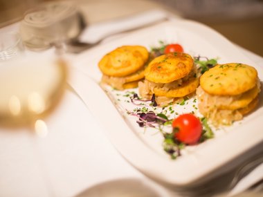 Three small savory sandwiches with greens and cherry tomatoes on a white plate