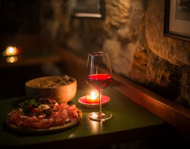 Glass of red wine and antipasti lit by candle on green table