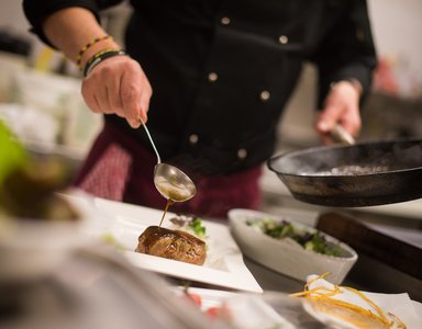 Koch schöpft Sauce auf ein Steak auf einem weißen Teller in der Küche