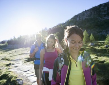 Drei Wanderer auf einem sonnigen Bergweg mit Rucksäcken und Sportkleidung