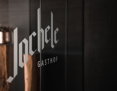 Glaswand mit Aufschrift Johle Gasthof und Holzdeko im Hintergrund