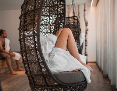 Personen in Bademänteln entspannen in einer Sauna mit Korbsesseln