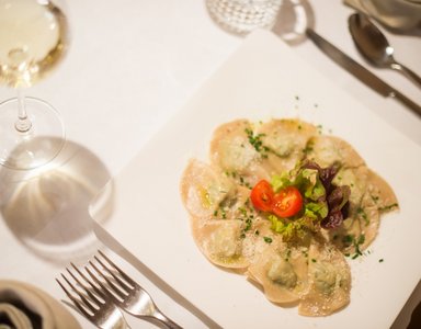 Teller mit Ravioli, garniert mit Tomaten und Salat, Weinglas und Besteck