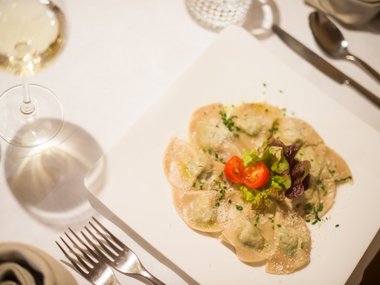 Plate of ravioli with tomatoes and salad, wine glass and cutlery