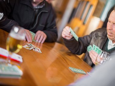 Uomini anziani che giocano a carte a un tavolo di legno con bevande