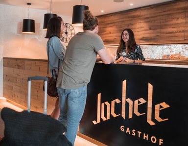 Gäste sprechen freundlich mit Mitarbeiterin an der Rezeption im Gasthof Jochele