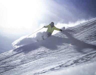 Skifahrer in gelber Jacke fährt schnellen Schwung den verschneiten Hang hinab