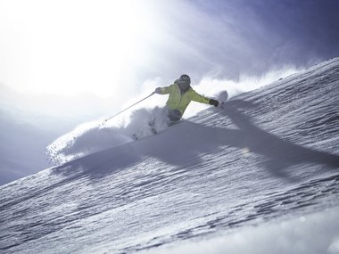 Sciatore con giacca gialla scende velocemente una pista innevata